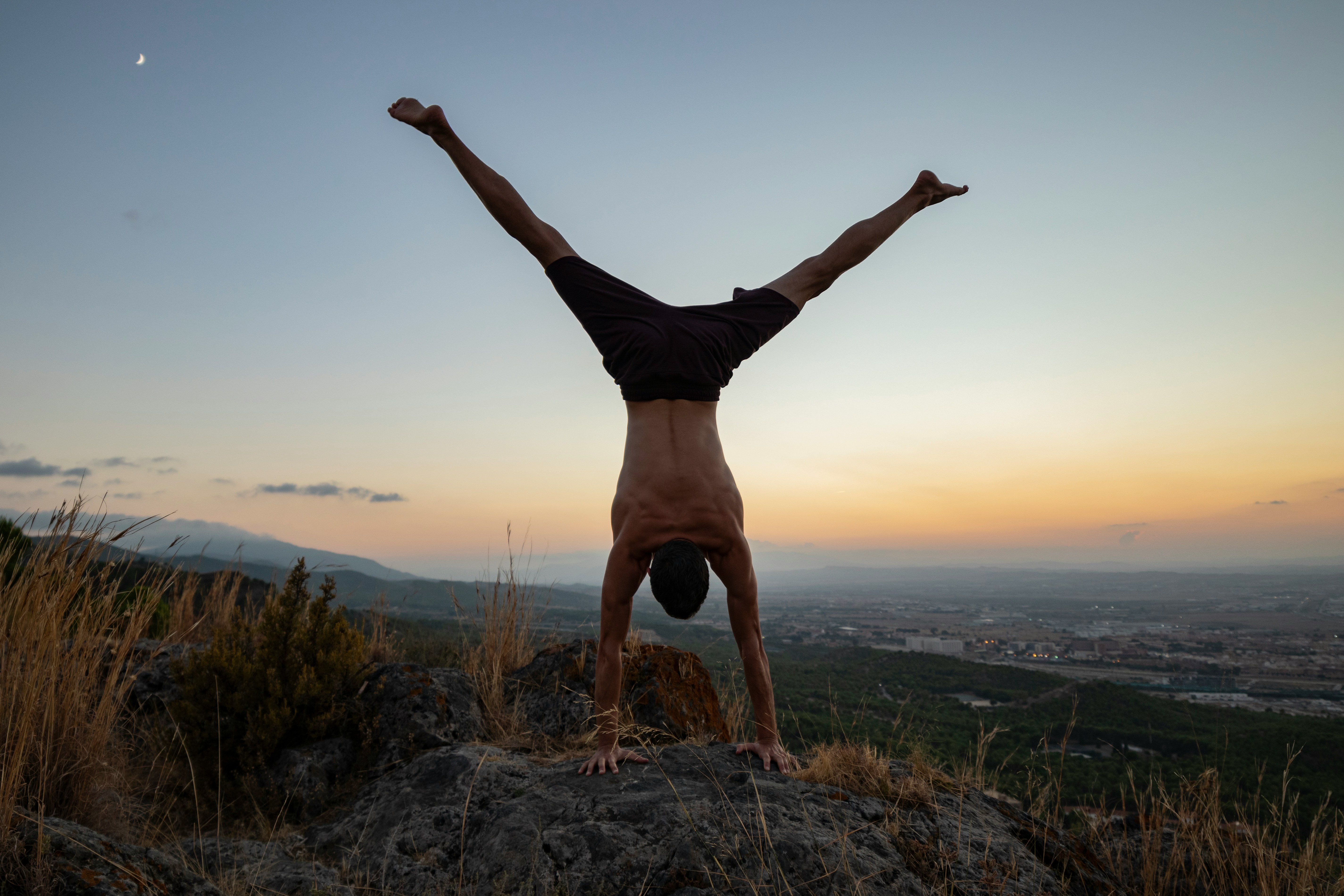 Person wearing a black outfit doing a handstand against a vivid blue sky with clouds in the background.